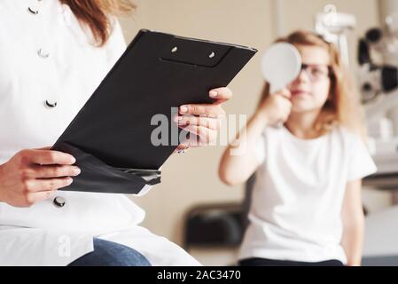 La conception de la santé de l'œil. Femme avec des tests d'acuité visuelle les documents de petite fille Banque D'Images