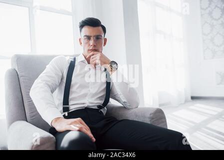 La photo en gros plan de guy attrayant dans les verres et élégant porter assis sur la chaise Banque D'Images
