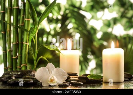 Grean feuilles de bambou, orchidée, fleur blanche, serviette et des bougies sur les pierres zen noir sur fond de feuilles tropicales Banque D'Images