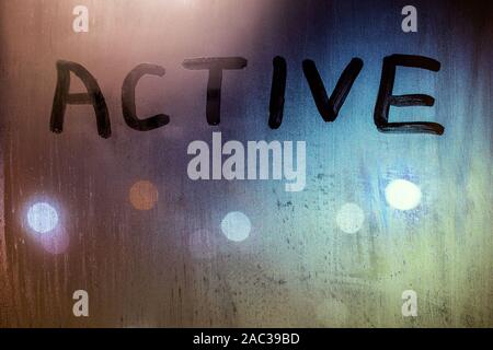 Le mot actif écrit sur la vitre humide nuit close-up avec l'arrière-plan flou. Banque D'Images