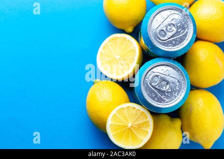 Les canettes de soda avec des gouttes de condensation et de citrons sur fond bleu Banque D'Images