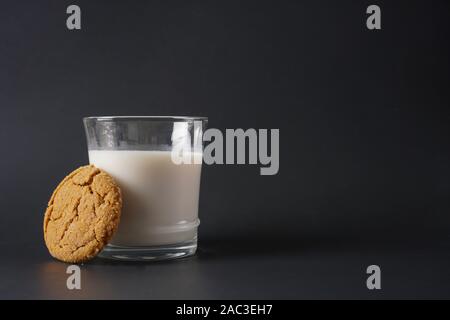 A gingerbread cookie se presse contre un verre de lait froid sur un fond noir avec copie espace sur le côté droit Banque D'Images