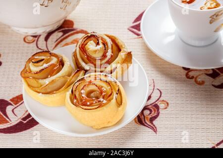 Trois Pains ruddy sur une soucoupe blanche avec apple à base de thé dans une tasse et une théière dans l'arrière-plan. Banque D'Images