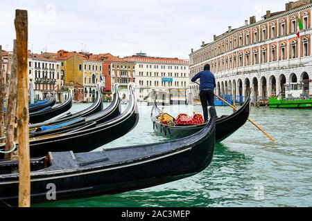 Un gondolier gondoles sa direction passé une ligne de bateaux amarrés sur le Grand Canal à Venise Italie Banque D'Images