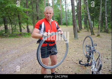 Un homme répare un vélo dans la forêt, une roue crevée au vélo, région de Kaliningrad, Russie, 31 juillet 2019 Banque D'Images