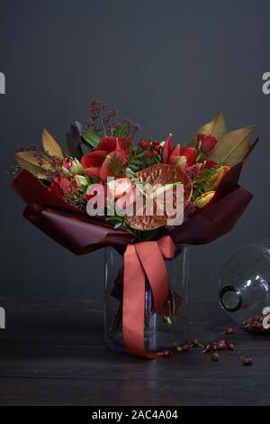 Bouquet d'automne chic en rouge les couleurs dans le style vintage dans un vase en verre et un énorme pot d'églantier à sec sur un fond sombre, selective focus Banque D'Images