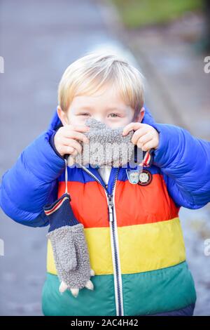 Cache-cache Le garçon est joué dehors dans les vêtements de plein air il est couvrant le visage et se cacher en regardant la caméra
