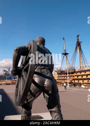 AJAXNETPHOTO. PORTSMOUTH, Angleterre. - Chantier naval HISTORIQUE STATUE EN BRONZE - UN CHAMP GUNNER REPRÉSENTÉ TRANSPORTER UNE ROUE DE CANON DE CAMPAGNE PAR SCULPTEUR BRITANNIQUE CHRISTOPHER KELLY. La STATUE SUR UN SOCLE COMMÉMORE LES HOMMES DE PORTSMOUTH DANS LE CANON DE CAMPAGNE ANNUELLE DE LA CONCURRENCE AU TOURNOI ROYAL ET QUI SE SONT ENTRAÎNÉS À LA CASERNE DE LA MARINE ROYALE DE 1947-1999 LORSQUE LE TOURNOI EST TERMINÉ. À LA LIMITE ET AU-DELÀ. NELSON'S 1805 BATAILLE DE TRAFALGAR NAVIRE AMIRAL HMS Victory est vu l'arrière-plan. PHOTO:JONATHAN EASTLAND/AJAX REF:GR110111 3169 Banque D'Images