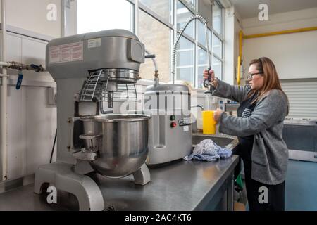 Une dame reçoit de l'eau dans une cruche d'un robinet dans une cantine cuisine. L'équipement, y compris un robot industriel s'asseoir sur un plan de travail en acier inoxydable. Banque D'Images