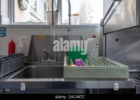 Un bac d'un lave-vaisselle industriel est situé sur le côté d'un lavabo dans une école cuisine. Banque D'Images