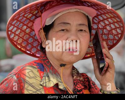 Personnes âgées vendeuse chinoise thaïlandaise traditionnelle Asiatique porte un chapeau conique et passe un appel sur son téléphone cellulaire. Banque D'Images