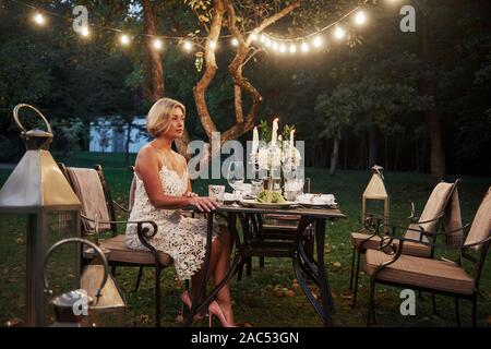 Femme adulte est assis sur la chaise avec des bougies et des verres à vin dans la partie extérieure du restaurant Banque D'Images