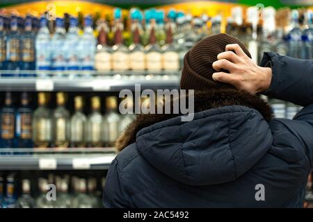 Yekaterinburg, Russie - Novembre 2019. Un homme en pensée devant les rangées de l'alcool dans un supermarché. Une large gamme de boissons alcoolisées. L'acheter Banque D'Images