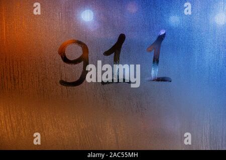 Le mot 911 pour united states service d'urgence écrit par doigt humide sur verre avec lumières floues en arrière-plan Banque D'Images