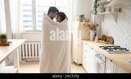 Young affectionate couple standing in kitchen enveloppé d'une couverture Banque D'Images