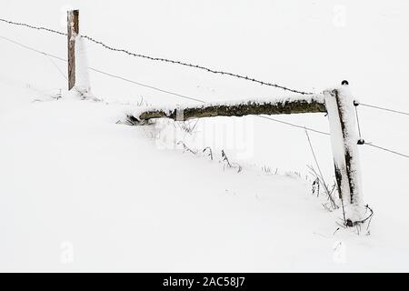 Poteau de clôture en bois avec du fil de fer barbelé sur un pâturage recouvert de neige Banque D'Images