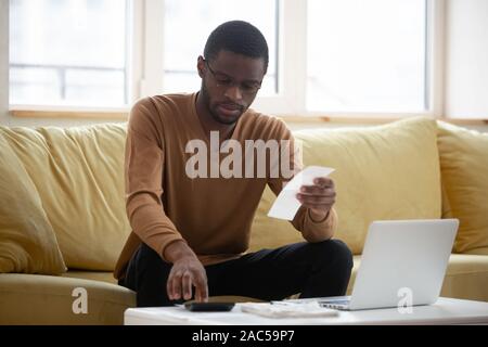 Homme biracial concentré le calcul des dépenses des ménages à la maison Banque D'Images