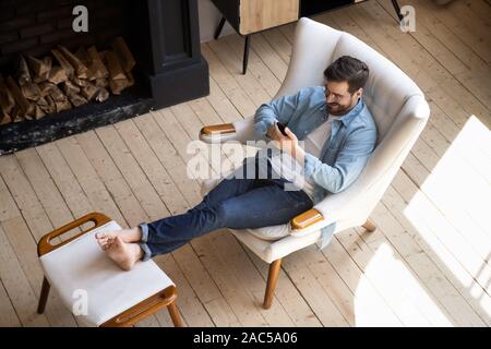Guy détendue s'asseoir sur une chaise confortable dans la chambre à l'aide de Phone Banque D'Images