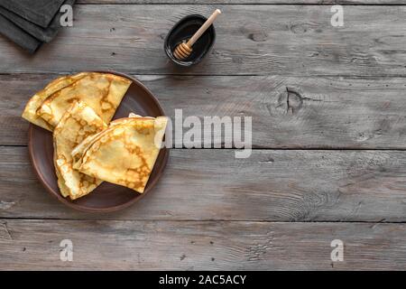 Crêpes avec du miel sur fond de bois rustique, vue du dessus, copiez l'espace. Des crêpes fines sur la plaque pour le petit-déjeuner ou un dessert. Banque D'Images