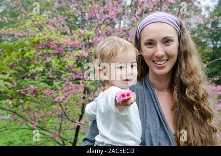 Une jeune mère et son Un-année-vieux fils offrir une fleur de cerisier avec un sourire, Big Island. Banque D'Images