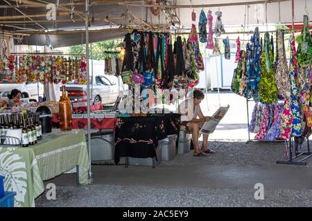 Un tissu local vendeur lit un journal à l'Hilo Farmers Market sur la rue Mamo, Grande Île d'Hawai'i. Banque D'Images