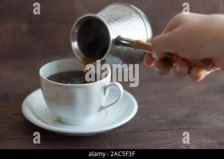 Une main d'homme est titulaire d'un Turc et verse du café fraîchement moulu dans une tasse Banque D'Images