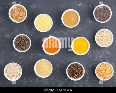 Le sarrasin, le millet, le piment, le fenouil, l'avoine, le poivre piment, masala, fenugrec, girofle, curcuma, cumin, graines de moutarde, la cardamome verte en blanc bols sur bl Banque D'Images