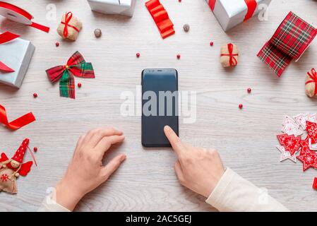 Touchez l'écran du téléphone à la main vide sur un bureau en bois entouré de décorations de Noël et des cadeaux. Concept de magasinage en ligne à l'époque de Noël. Vue d'en haut Banque D'Images