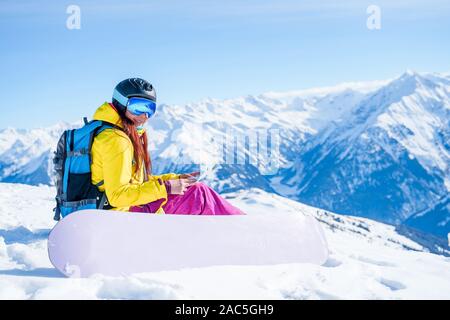 Photo de snowboarder girl à casque avec la carte dans ses mains, assis sur la montagne en hiver Banque D'Images