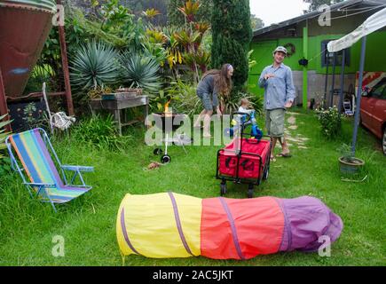 Une jeune mère, père et enfant fils jouer dans leur cour, en commençant avec un barbecue et des jouets éparpillés, Big Island. Banque D'Images