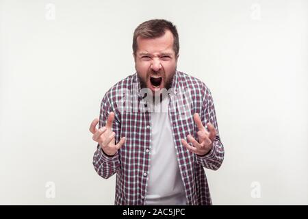 Portrait de jeune homme barbu agressif en chemise à carreaux avec permanent furieux visage plein de haine et de colère, des émotions fortes, je cris. Banque D'Images