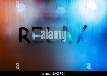 Le mot vous détendre écrit par doigt humide sur verre avec lumières floues en arrière-plan. Banque D'Images