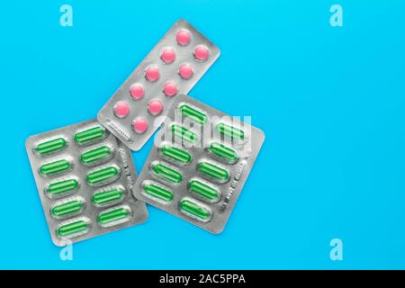 Distributeur de pilules sur un fond bleu. Copier l'espace. Blisters de comprimés roses et verts de capsules. Concept de la médecine. Banque D'Images