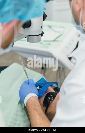 Médecin utilisé microscope. Dentiste est de traiter le patient en cabinet dentaire moderne. L'opération est réalisée à l'aide de batardeau. Client est inséré et restauré Banque D'Images