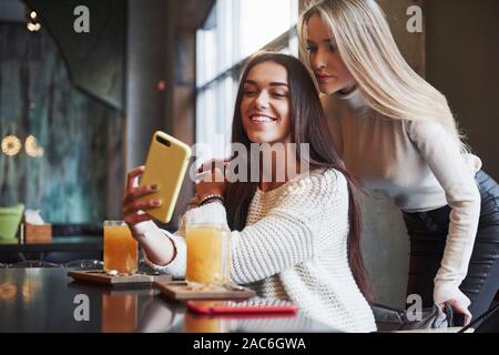 Prenons la photo. Dans le restaurant. Deux amies, m'asseoir à l'intérieur avec verre jaune et utiliser le smartphone Banque D'Images