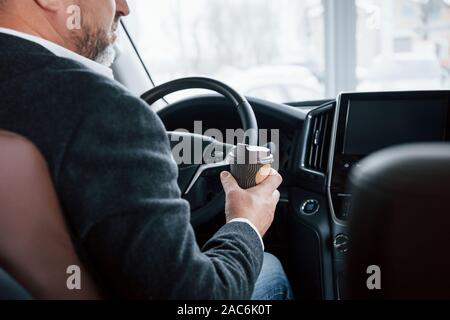 Tasse à café. est Vue de derrière de senior businessman dans les vêtements à l'intérieur de voiture moderne Banque D'Images