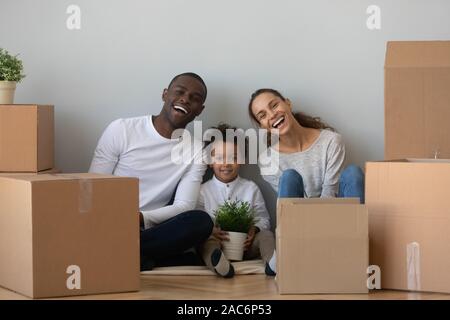 Heureux mixed race family sitting on floor près de boîtes de carton. Banque D'Images