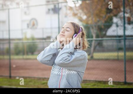 Belle jeune fille adolescente à la mode est à l'écoute de la musique sur le casque du smartphone Banque D'Images