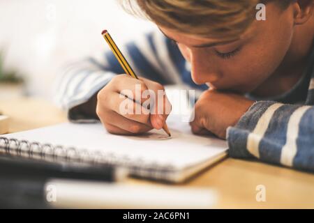 Dessin au crayon d'étudiants sur l'ordinateur portable. Boy doing homework écrit sur un papier. Kid tenir un crayon et dessiner un manga à la maison. Une séance de dessin de l'adolescence Banque D'Images