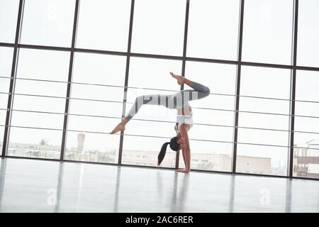 Doing handstand. Vue de côté de fille en faisant des exercices stretch sportswear dans la grande salle de sport spacieuse Banque D'Images