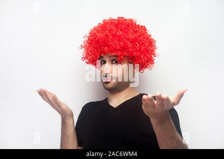 Ne sais pas, qui s'en soucie. Portrait de l'homme bizarre drôle en poils bouclés et avec la perruque rouge dans les mains de perplexité, à la confondre avec l'indigne exp Banque D'Images