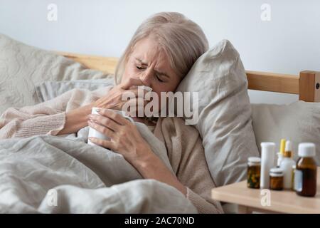 Vieille Femme au lit soufflant le nez dans un mouchoir Banque D'Images