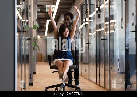 Collègues having fun riding assis sur une chaise dans le couloir du bureau Banque D'Images