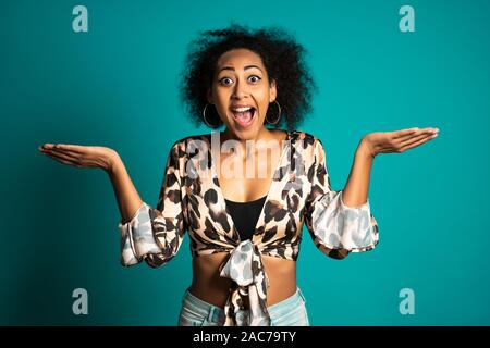 Pretty african american woman avec les cheveux afro dans Leopard porter smiling, agréablement surpris à l'appareil photo sur mur bleu arrière-plan. Banque D'Images