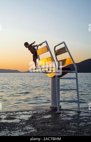 Garçon saute sur le tremplin d'une plateforme de plongée dans la mer Méditerranée sur l'île de Cres dans la baie de Kvarner, Croatie, au coucher du soleil Banque D'Images