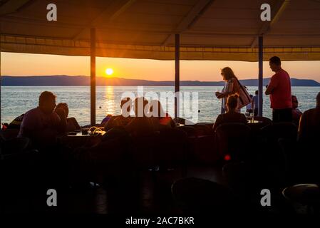 Invités dans un restaurant en bord de mer sur l'île de Cres voir le coucher du soleil sur la baie de Kvarner, Croatie Banque D'Images