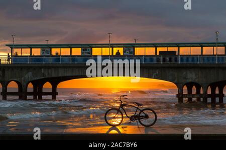Bournemouth, Dorset UK. 1er décembre 2019. Météo France : magnifique coucher de soleil à la plage de Bournemouth à la fin d'un froid glacial d'hiver ensoleillé sec 24. Vélo, vélo, sur le bord de la mer qui se profile dans le coucher du soleil encadré par la jetée. Credit : Carolyn Jenkins/Alamy Live News Banque D'Images