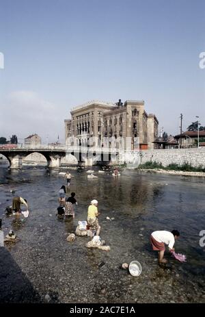 9 août 1993 pendant le siège de Sarajevo : les femmes laver la lessive dans la rivière Miljacka, avec l'holocauste de National Art Gallery et de la bibliothèque à l'arrière-plan. Aujourd'hui, la Bibliothèque est l'Hôtel de ville de Sarajevo. Banque D'Images