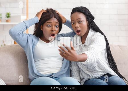 Choqué Black Girls Looking At Smartphone la lecture à l'écran Message inattendu Banque D'Images