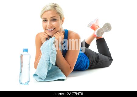 Jeune fille dans un uniforme de sport se trouve sur un tapis de yoga avec une serviette sur un fond blanc. Banque D'Images